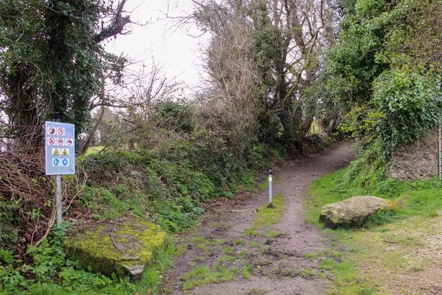 a sign on a dirt path in a wooded area