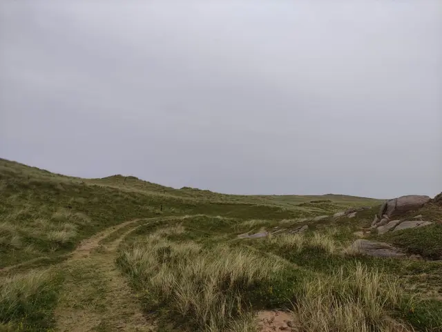 a grassy hill with rocks and the walking trail