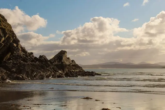 a beach with a rocky cliff and water with a blue sky