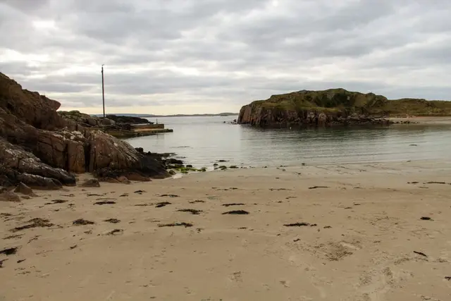 a sandy beach with a body of water and a land with rocks