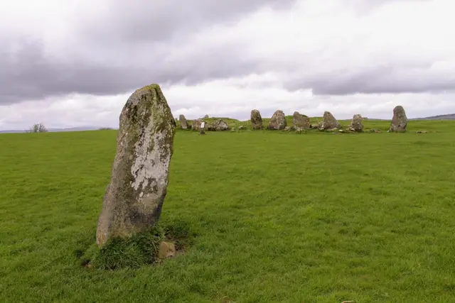 a grassy field with rocks in it with Avebury in the background