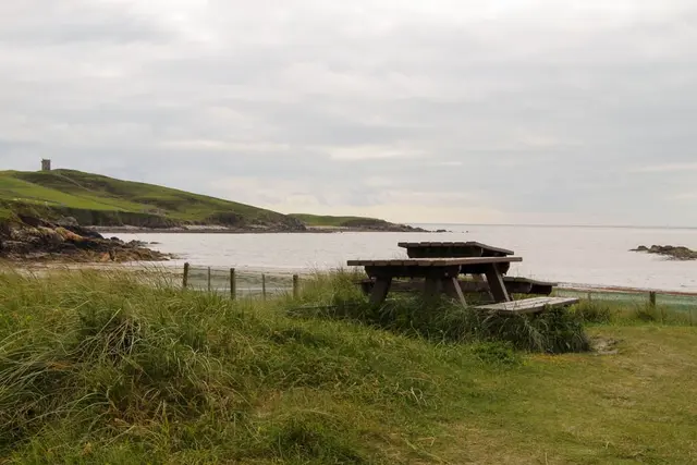 a picnic table on a grassy hill by a body of water