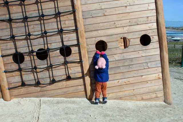 a child standing in front of a wooden fence with a baby in it