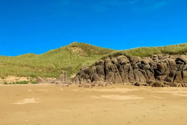 a rocky hill with grass and sand